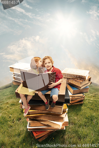 Image of Little girl and boy sitting on the tower made of big books