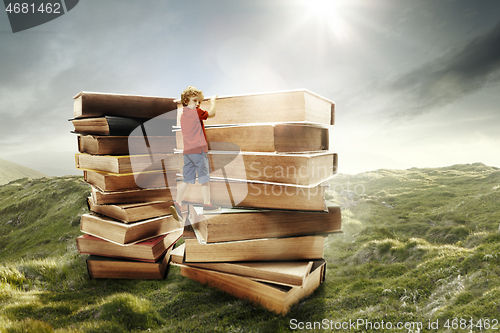 Image of Little boy climbing on the tower made of big books