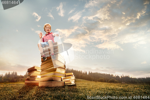 Image of Little boy sitting on the tower made of big books