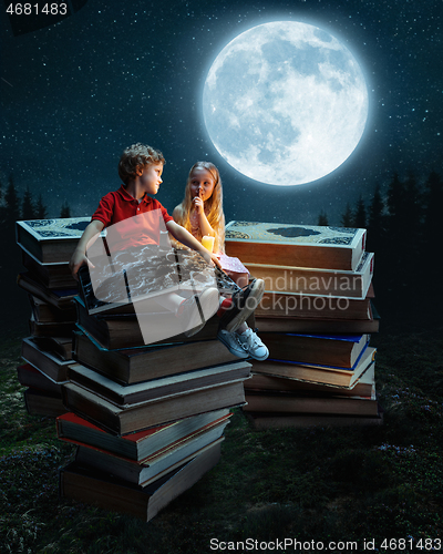 Image of Little girl and boy sitting on the tower made of big books