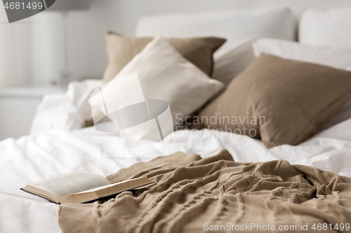 Image of bed with pillows, blanket and open book at home