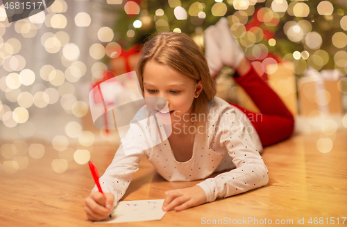 Image of smiling girl writing christmas wish list at home