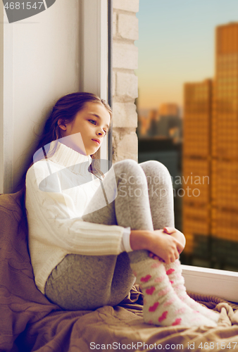 Image of sad girl sitting on sill at home window over city