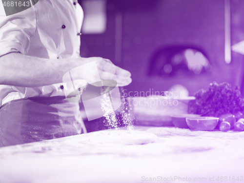 Image of chef sprinkling flour over fresh pizza dough