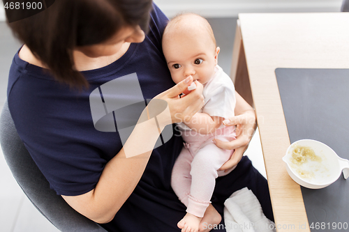 Image of middle-aged mother feeding baby daughter at home