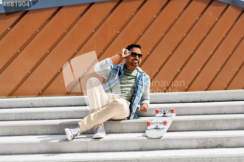 Image of indian man with skateboard sitting on city stairs