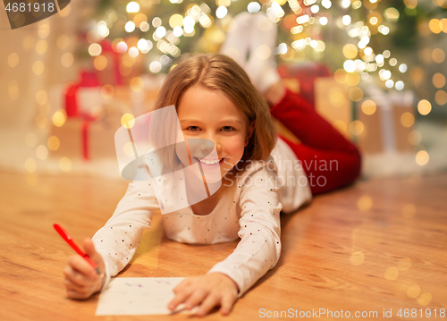 Image of smiling girl writing christmas wish list at home