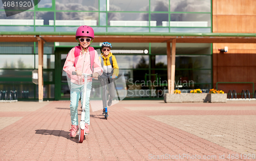 Image of happy school children riding scooters outdoors