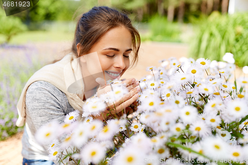 Image of happy woman smelling chamomile flowers in garden