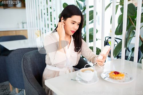 Image of asian woman with smartphone and earphones at cafe