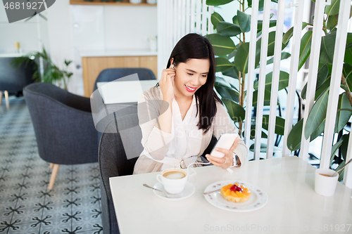 Image of asian woman with smartphone and earphones at cafe