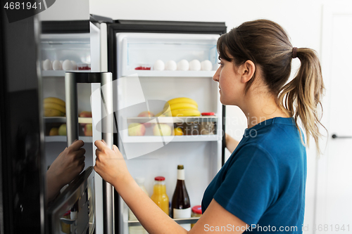 Image of woman at open fridge at home kitchen