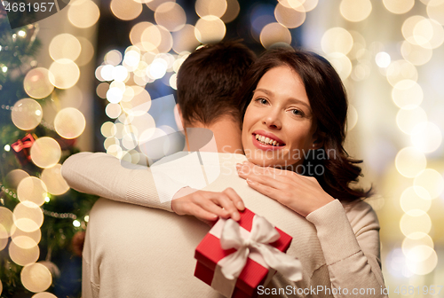 Image of happy couple with christmas gift hugging at home