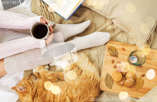 Image of woman with coffee and red cat sleeping in bed
