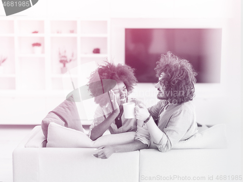 Image of multiethnic couple sitting on sofa at home drinking coffe