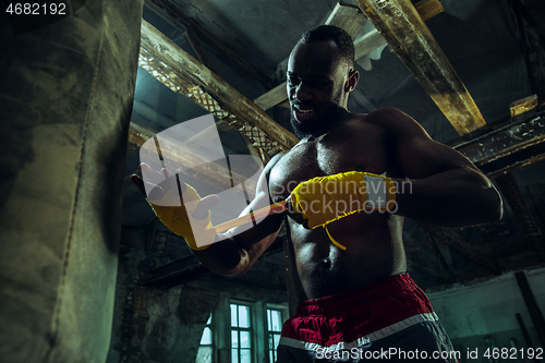 Image of Afro American boxer is wrapping hands with bandage