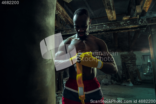 Image of Afro American boxer is wrapping hands with bandage