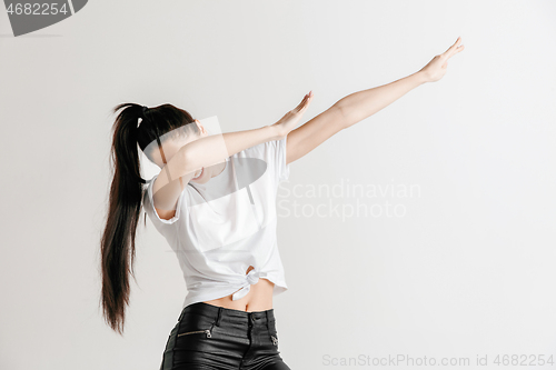 Image of Young woman makes the dab movement with his arms on a gray background.