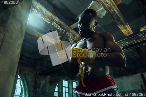 Image of Afro American boxer is wrapping hands with bandage