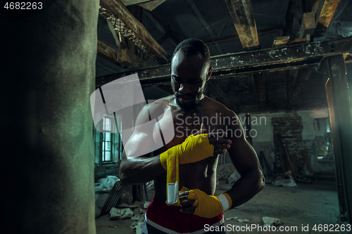 Image of Afro American boxer is wrapping hands with bandage