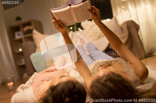 Image of happy female friends reading book at home