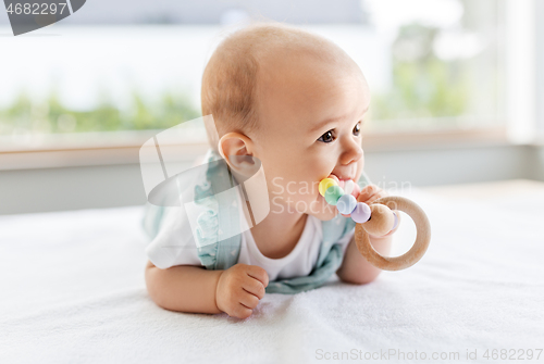 Image of baby girl on white blanket chewing wooden rattle