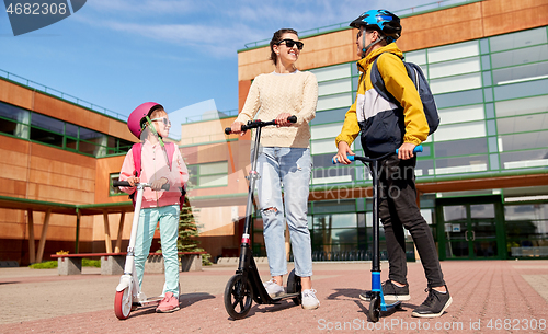 Image of happy school children with mother riding scooters