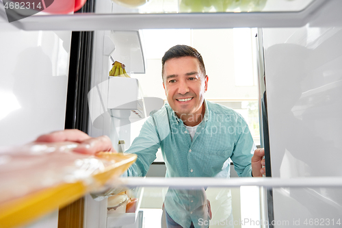 Image of man taking food package from fridge at kitchen