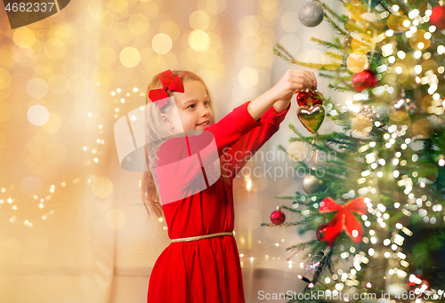 Image of happy girl in red dress decorating christmas tree
