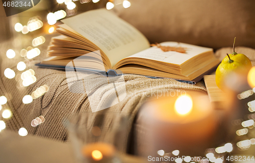 Image of book with autumn leaf and blanket on sofa at home