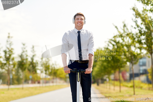 Image of businessman with headphones riding scooter in city