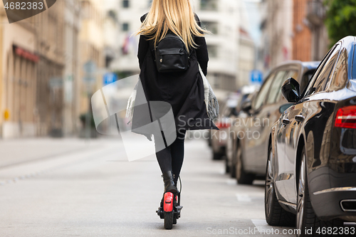 Image of Rear view of girl riding public rental electric scooter in urban city environment. New eco-friendly modern public city transport in Ljubljana