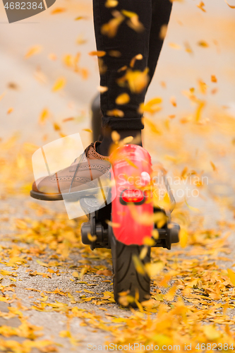 Image of Detail of fashinable hipster girl riding electric scooter in park at fall