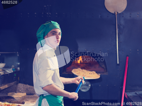 Image of chef putting delicious pizza to brick wood oven