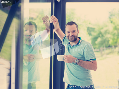 Image of young man drinking morning coffee by the window