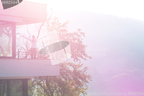 Image of woman stretching her arms on balcony