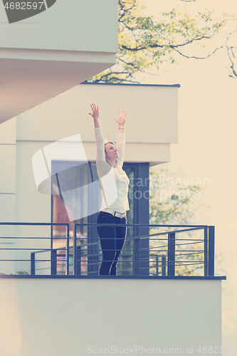 Image of woman stretching her arms on balcony