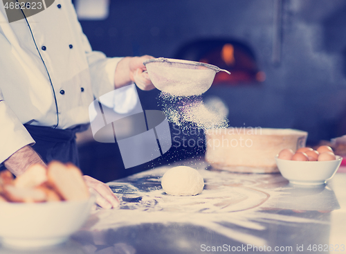 Image of chef sprinkling flour over fresh pizza dough