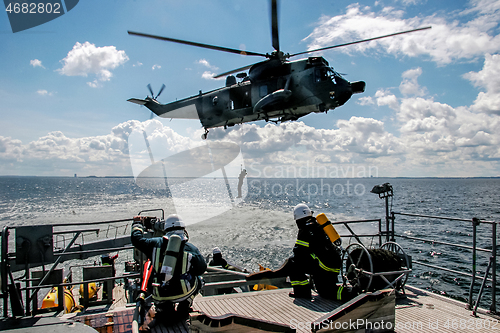 Image of NATO rescue mission in sea with ship and helicopter.