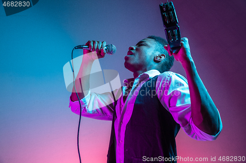 Image of African American handsome jazz musician playing tambourine and singing.