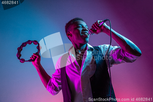 Image of African American handsome jazz musician playing tambourine and singing.