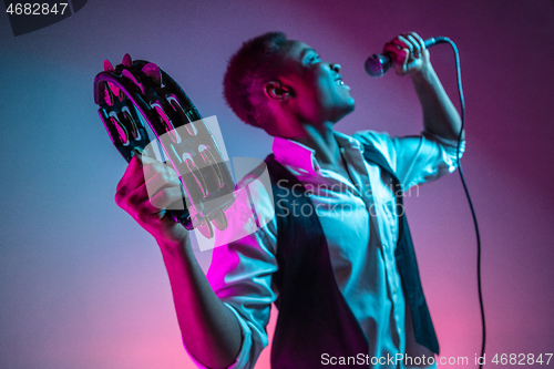 Image of African American handsome jazz musician playing tambourine and singing.