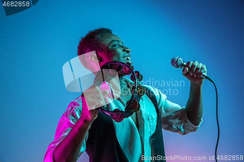 Image of African American handsome jazz musician playing tambourine and singing.