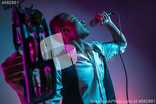 Image of African American handsome jazz musician playing tambourine and singing.