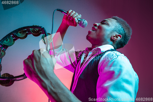 Image of African American handsome jazz musician playing tambourine and singing.