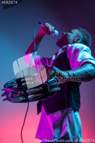 Image of African American handsome jazz musician playing tambourine and singing.