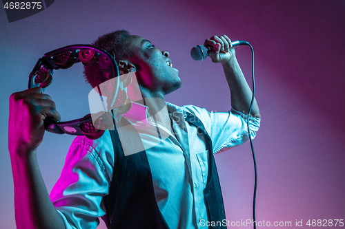 Image of African American handsome jazz musician playing tambourine and singing.