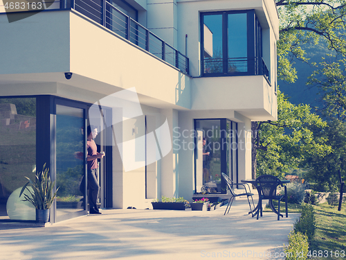 Image of man drinking coffee in front of her luxury home villa