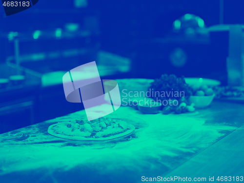 Image of chef putting fresh vegetables on pizza dough