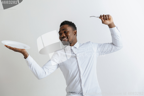 Image of Young smiling attractive african american guy holding empty dish and fork isolated on grey background. Copy space and mock up. Blank template background.